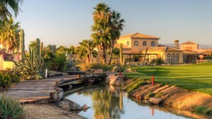 Un campo de golf con un estanque, palmeras y un edificio de estilo mediterráneo.