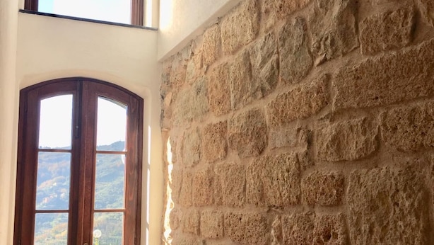 Ein Zimmer mit Steinwand und Holztür, die auf einen Balkon mit Blick auf die Landschaft führt.