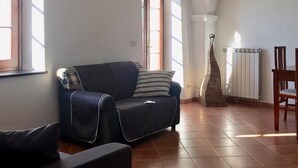 Ein gemütliches Wohnzimmer mit einem dunkelgrauen Sofa, einem Holzstuhl und einer Heizung.