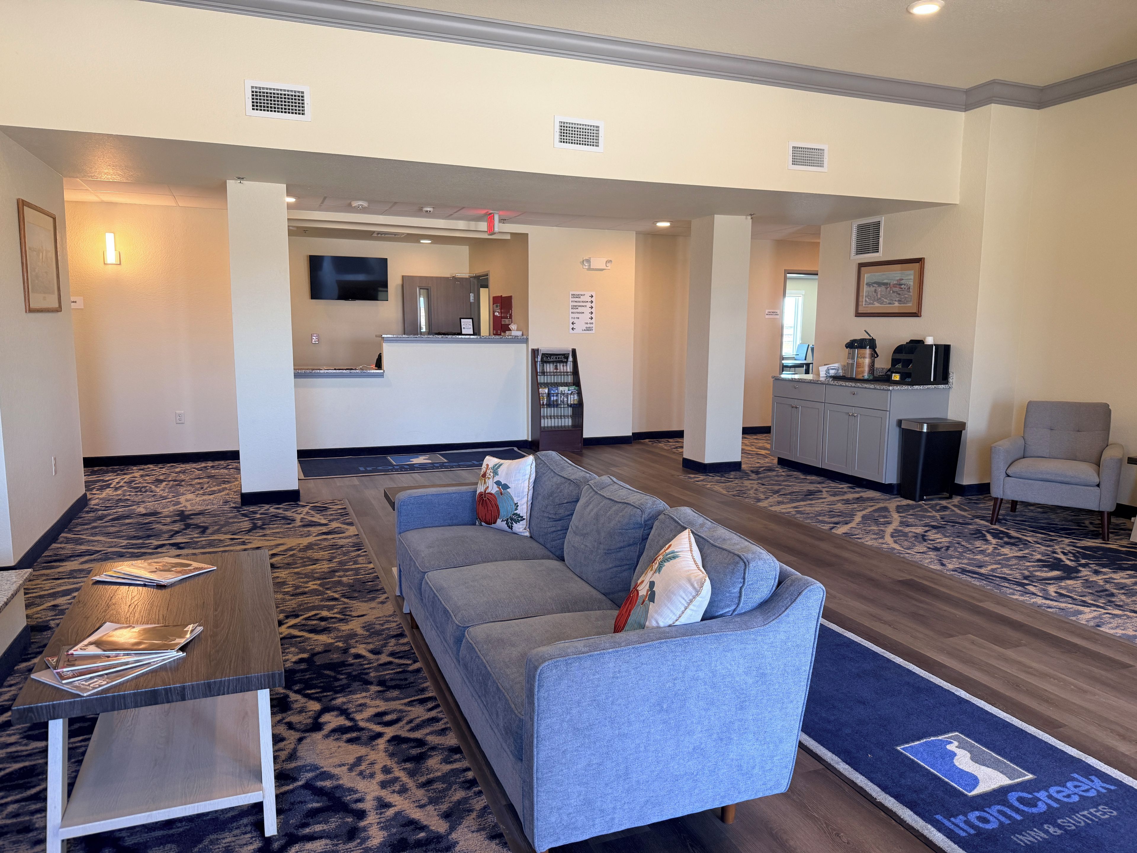 A hotel lobby with a reception desk, a seating area with a sofa and a coffee table, and a carpeted floor.