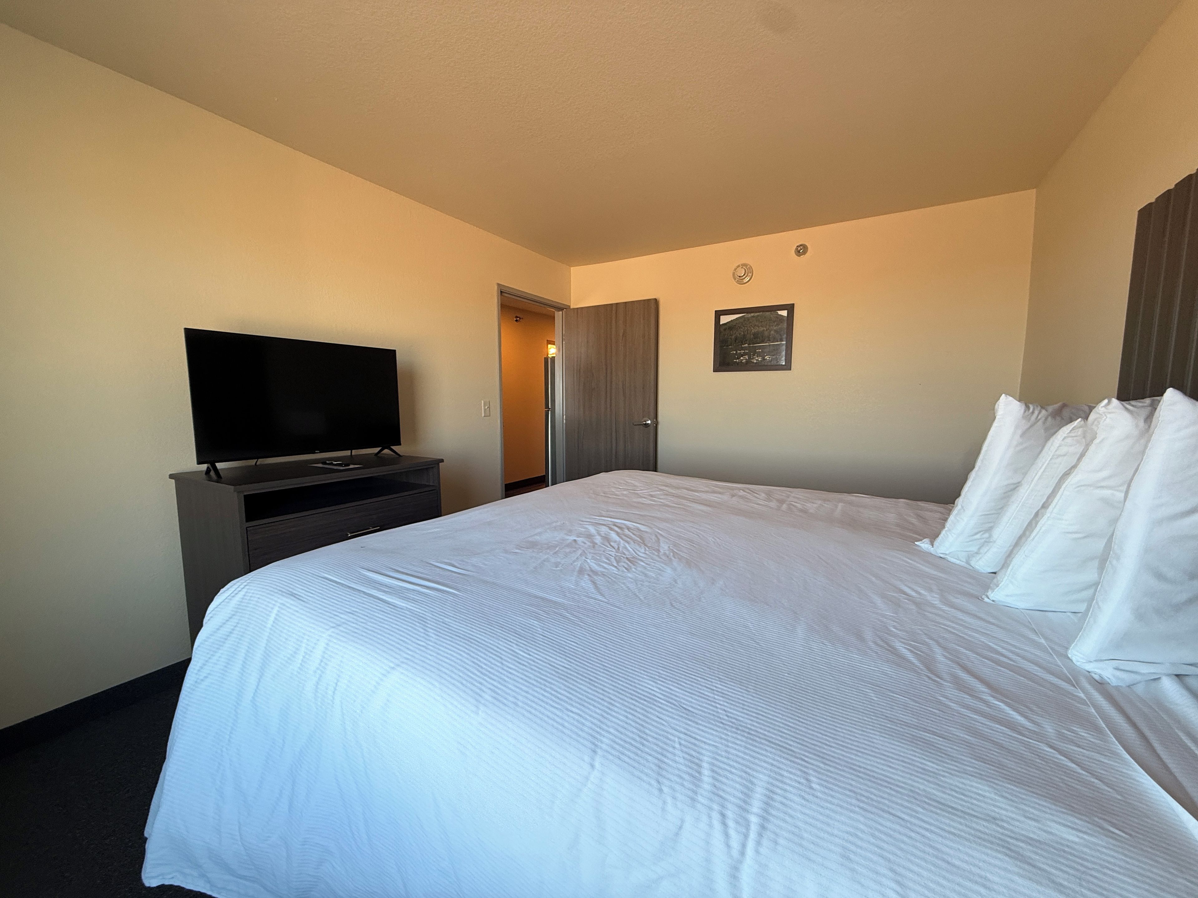 A hotel room with a large bed, a flat-screen TV on a dresser, and a door leading to another room.