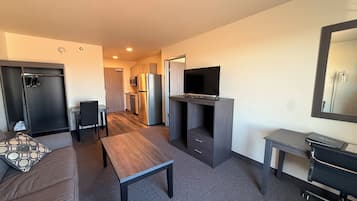 A compact hotel room with a sofa, a small table, a TV on a stand, a desk, and a wardrobe.