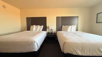 A hotel room with two beds, a nightstand, a lamp, and a wall-mounted picture.