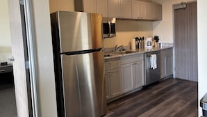A modern kitchen with stainless steel appliances, light wood cabinets, and a dark wood floor. - Iron Creek Inn & Suites (Upton)