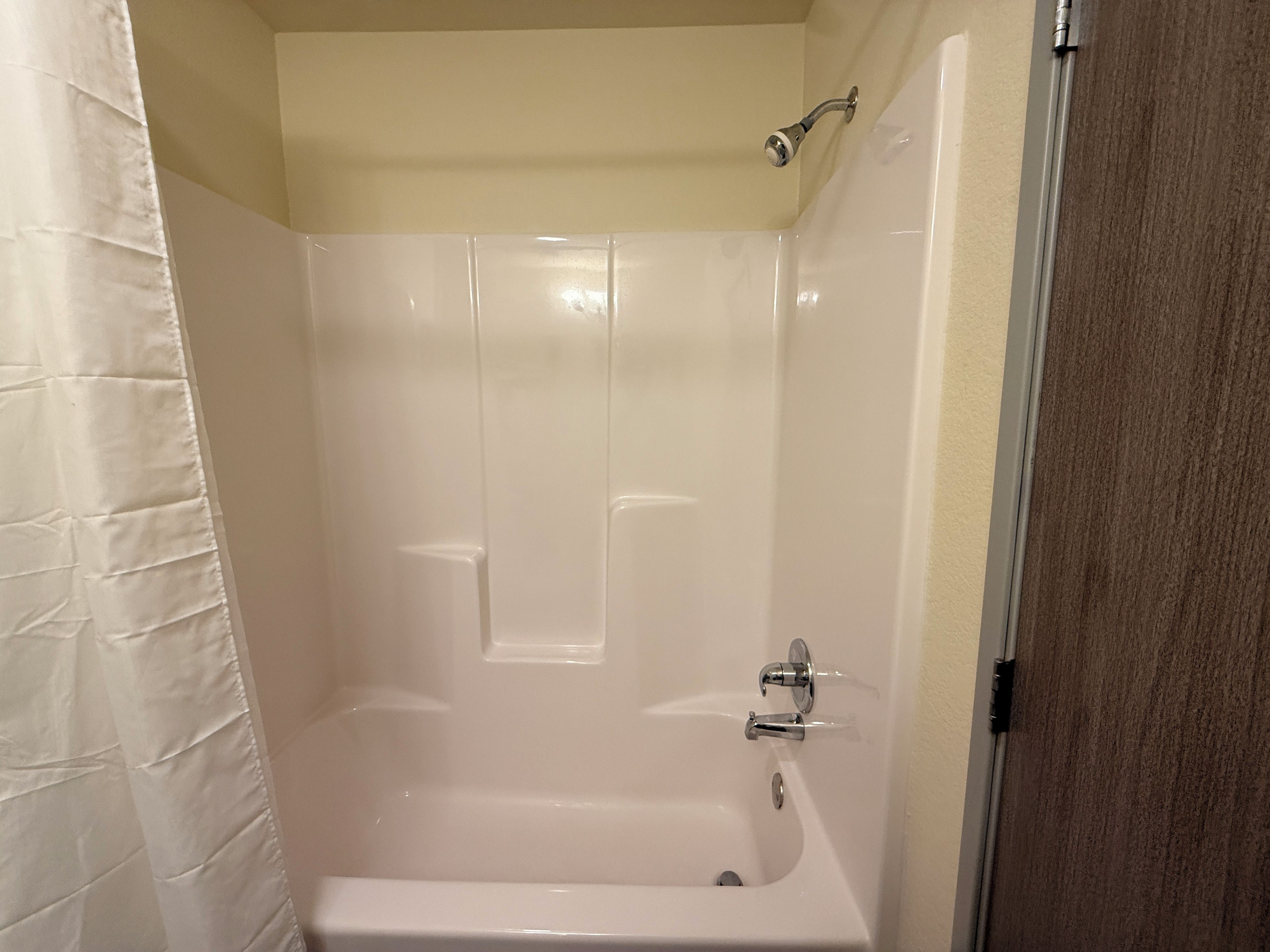 Un baño con una bañera blanca, cabezal de ducha y una puerta.