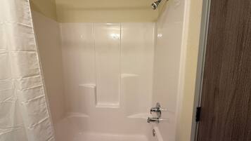 Un baño con una bañera blanca, cabezal de ducha y una puerta.