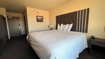A hotel room with a large bed, a headboard with vertical slats, a bedside table with a lamp, and a door leading to another room.