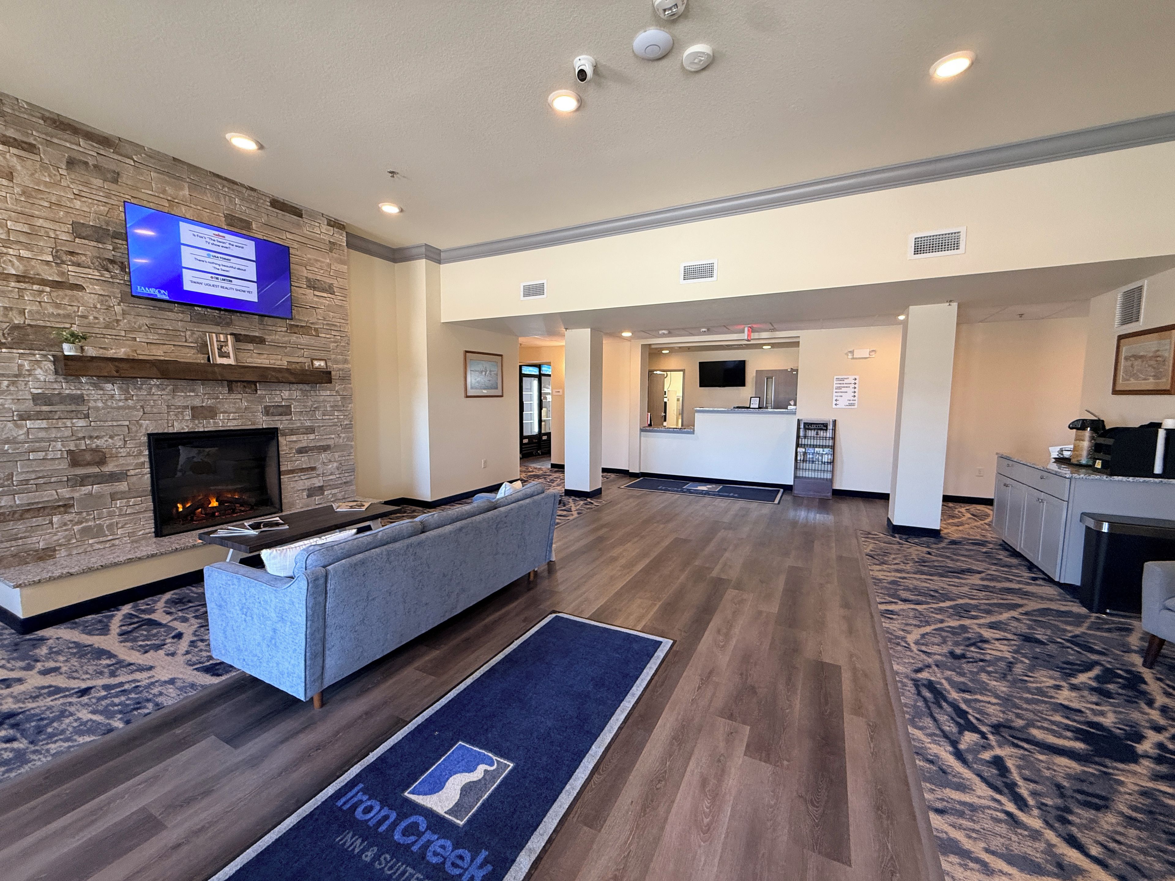 A hotel lobby with a stone fireplace, a flat-screen TV, a reception desk, and a seating area.
