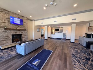 A hotel lobby with a stone fireplace, a flat-screen TV, a reception desk, and a seating area. - Iron Creek Inn & Suites (Upton)