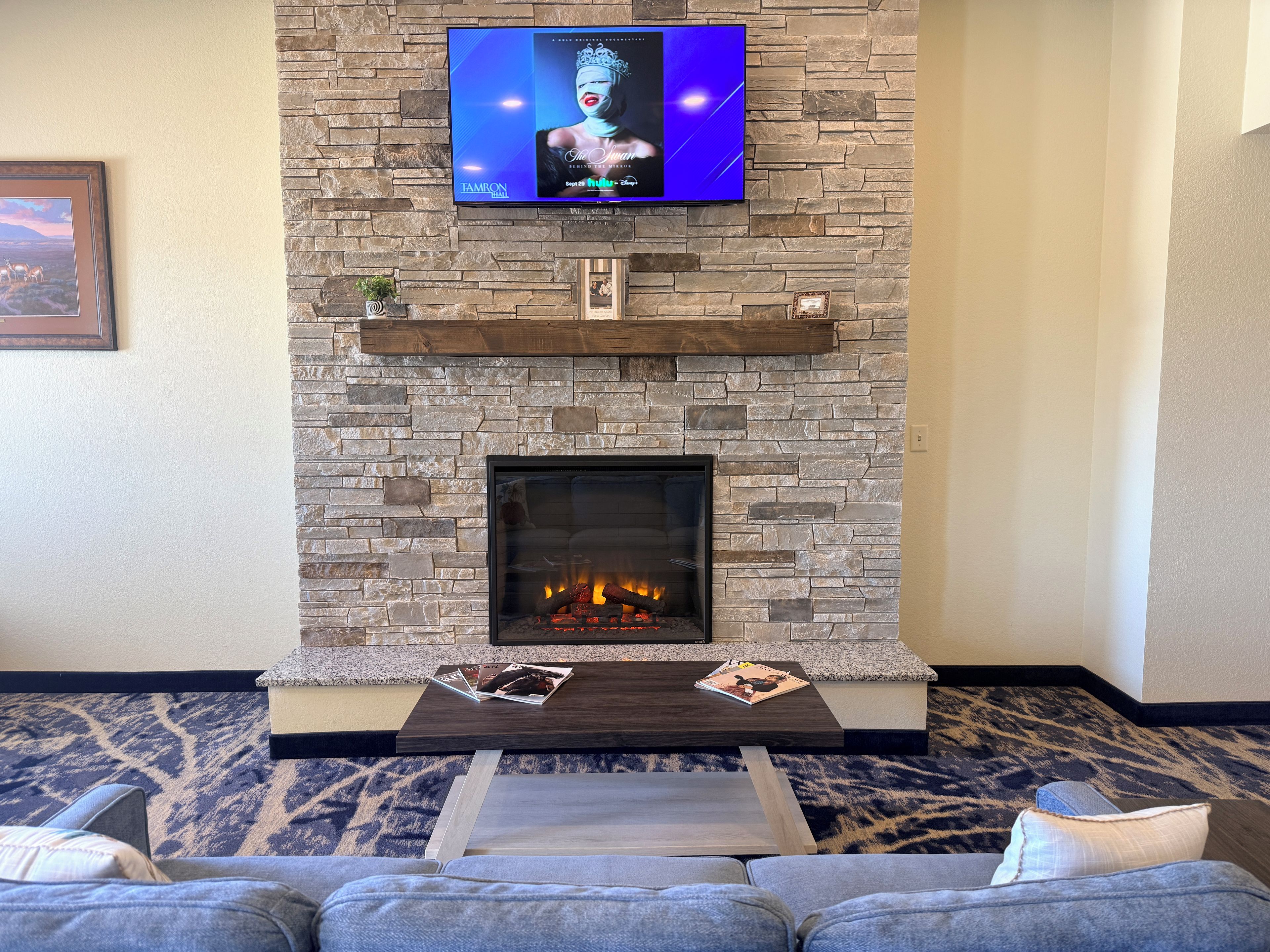 A living room with a stone fireplace, a flat-screen TV mounted above it, and a sofa with a patterned carpet.