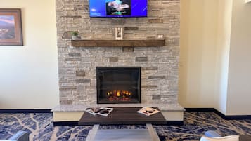 A living room with a stone fireplace, a flat-screen TV mounted above it, and a sofa with a patterned carpet.