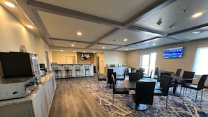 A hotel lobby with a bar area, seating, a kitchen, and a TV displaying the weather. - Iron Creek Inn & Suites (Upton)