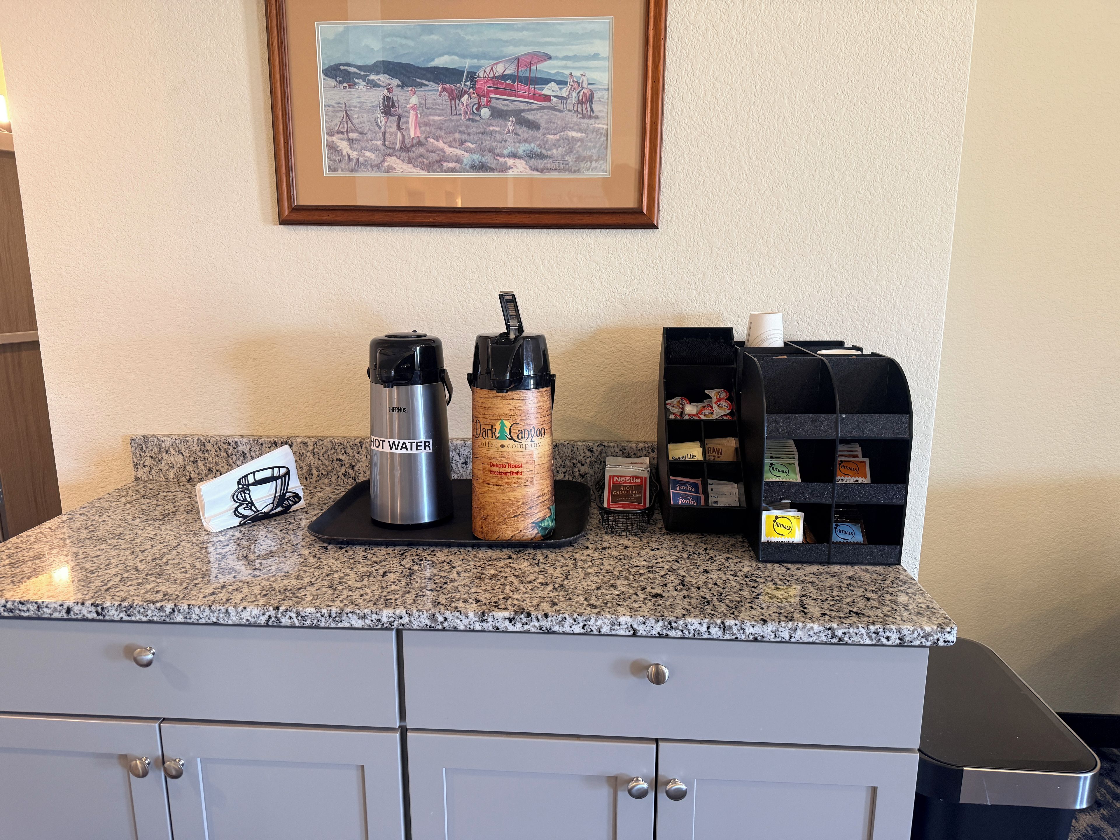A kitchen counter with a coffee maker, a thermos, a water bottle, and a coffee station.
