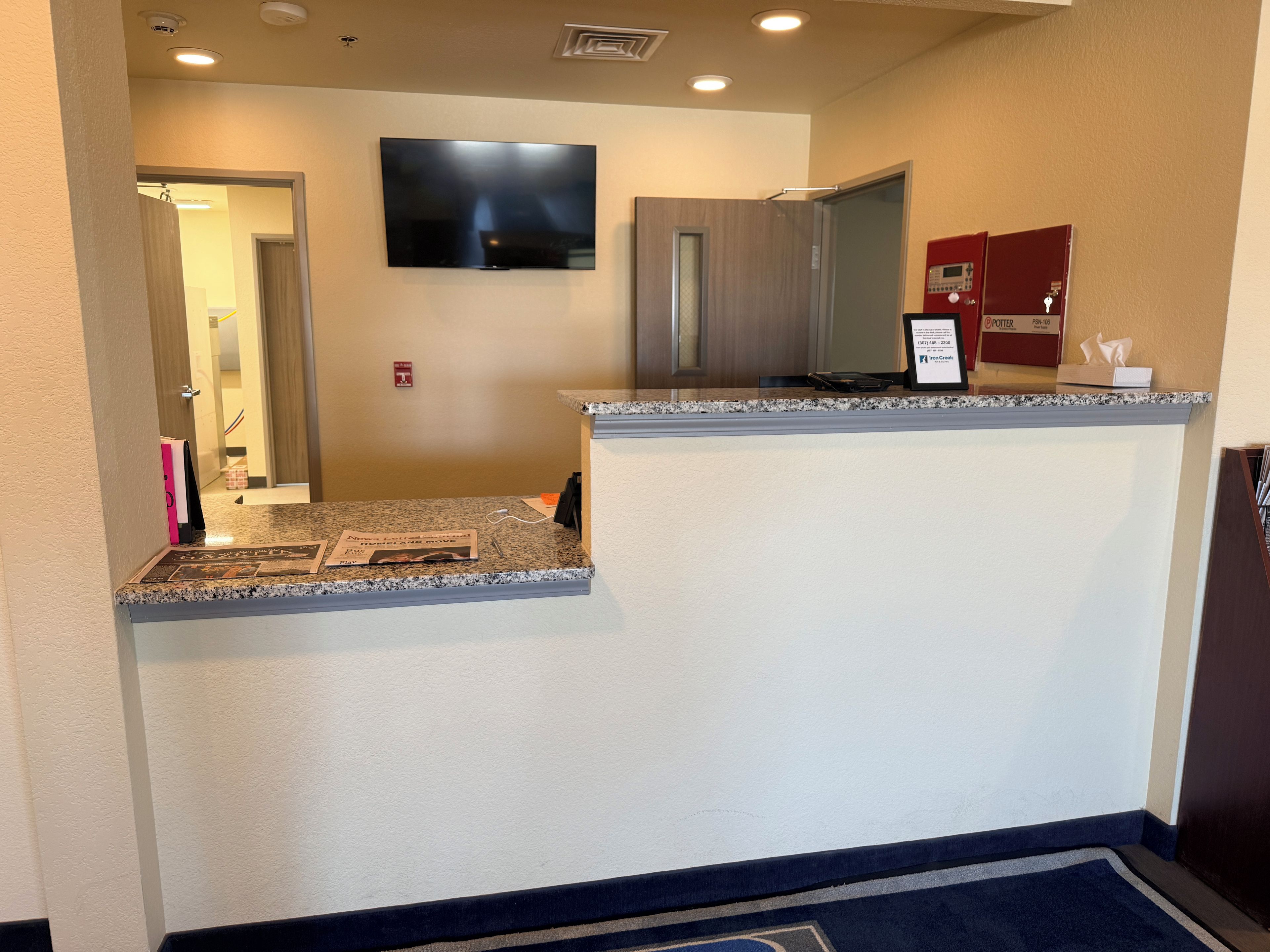 A hotel reception area with a flat-screen TV mounted on the wall, a reception desk with a granite countertop, and a microwave above it.