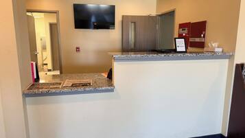 A hotel reception area with a flat-screen TV mounted on the wall, a reception desk with a granite countertop, and a microwave above it.