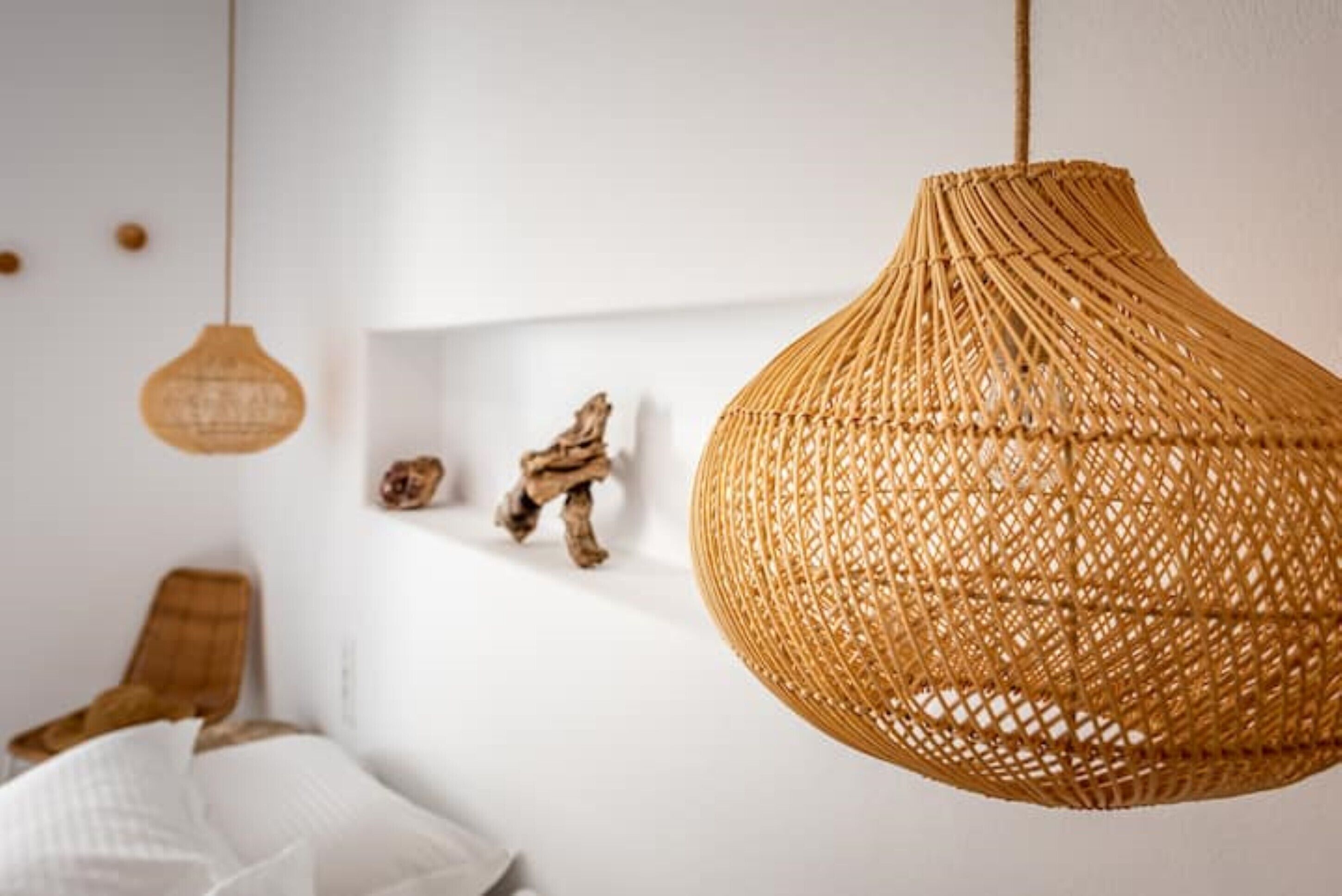 Een kamer met een grote geweven hanglamp, een bed met wit beddengoed en een klein decoratief object aan de muur.