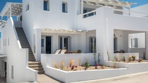 A modern white two-story house with a covered outdoor seating area and a staircase leading to the upper floor. - Elyos Apartment Ermes (milos)