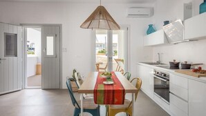 A modern kitchen with white cabinets, a dining table with a red table runner, and a hanging light fixture. - Elyos Apartment Ermes (milos)