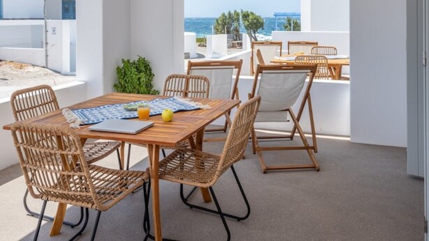 A modern outdoor dining area with wicker furniture and a view of the sea. - Elyos Apartment Ermes (milos)
