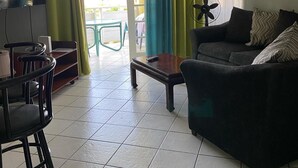 Una sala de estar con un sofá, una mesa de centro, un televisor y un ventilador. Hay una puerta que da a un espacio exterior.