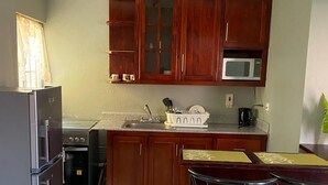 Una cocina compacta con armarios de madera, un microondas, un refrigerador y una pequeña barra con taburetes.