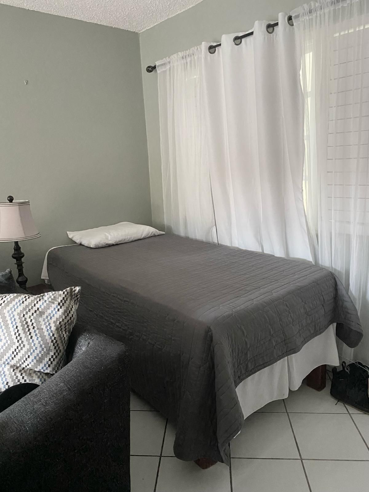 Une chambre à coucher avec un lit, une chaise, une lampe et une fenêtre avec des rideaux.
