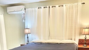 Una habitación de hotel con cama, cortinas, lámpara y aire acondicionado.