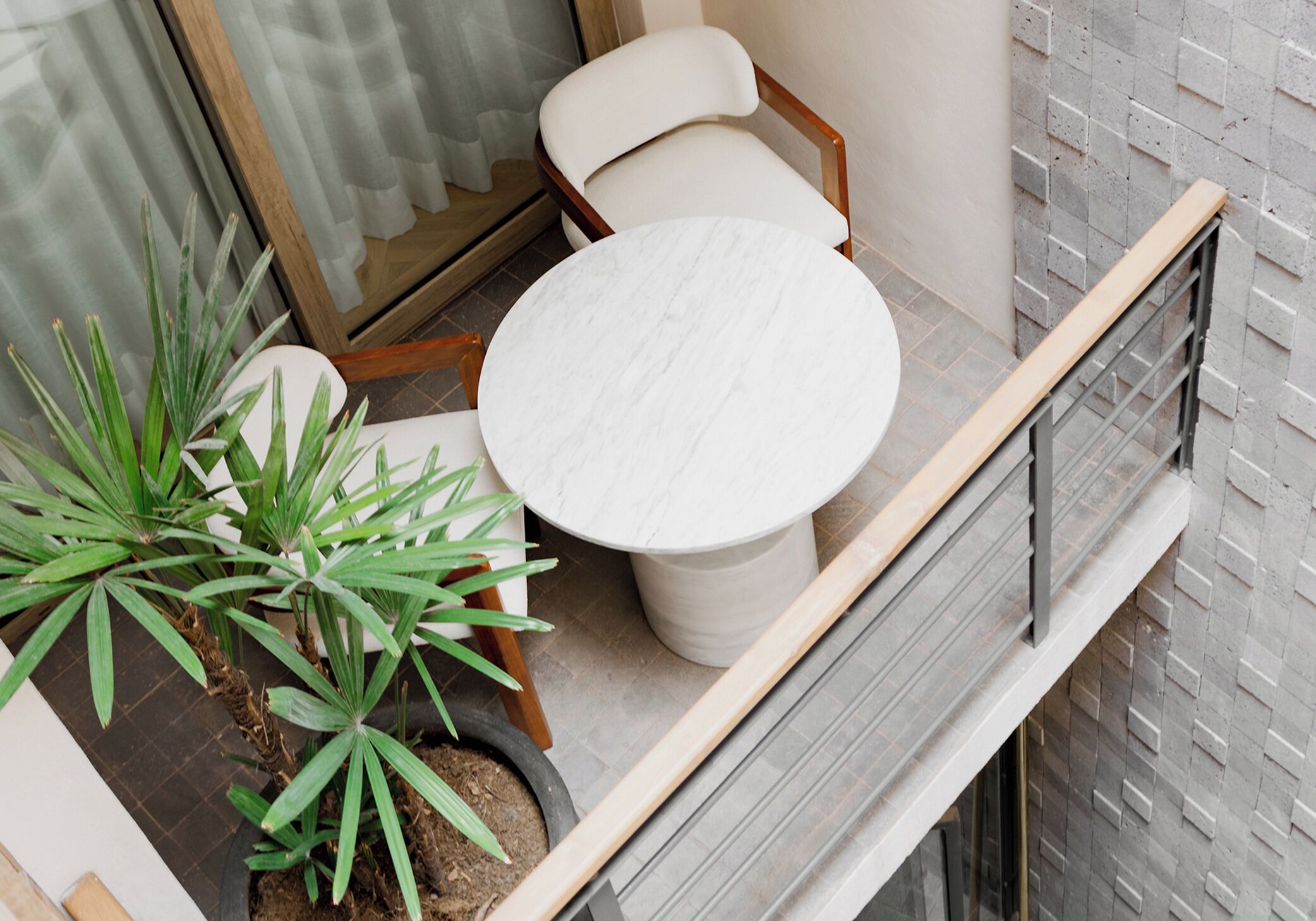 A balcony with a round table and two chairs, potted plants, and a view of the building's exterior.