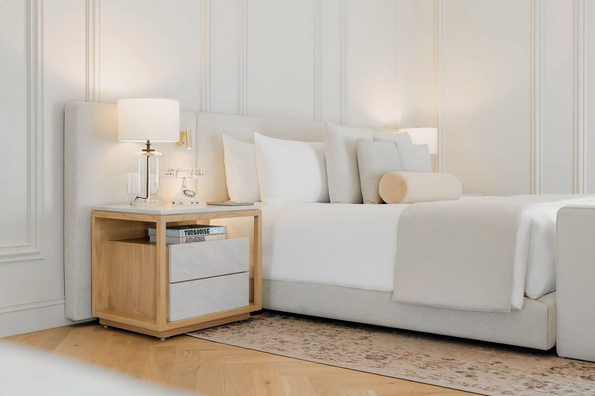Een netjes opgemaakt slaapkamer met een bed, nachtkastje, lamp en een klein houten kastje.