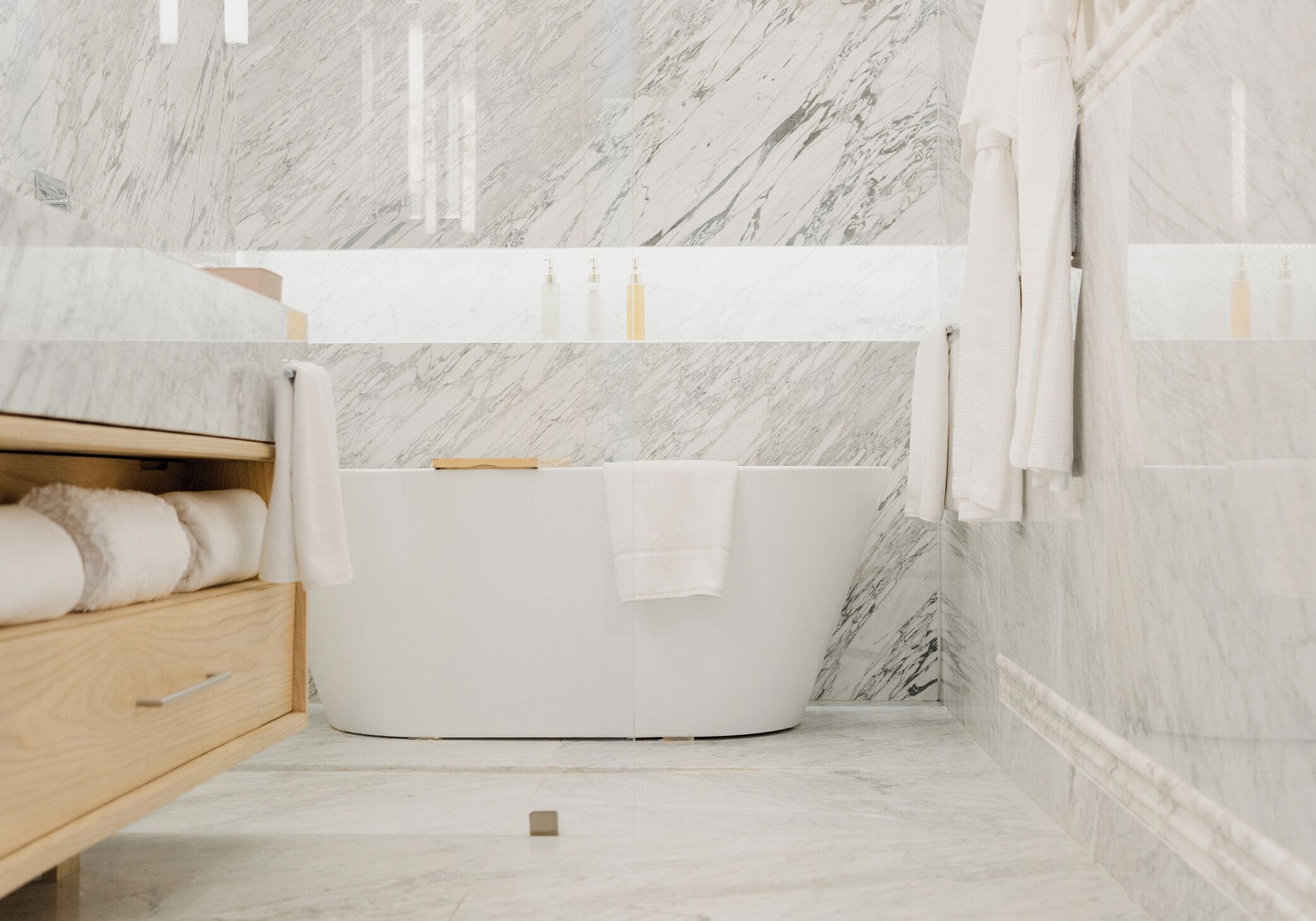Un baño moderno con una bañera independiente, tocador de madera y paredes de mármol.