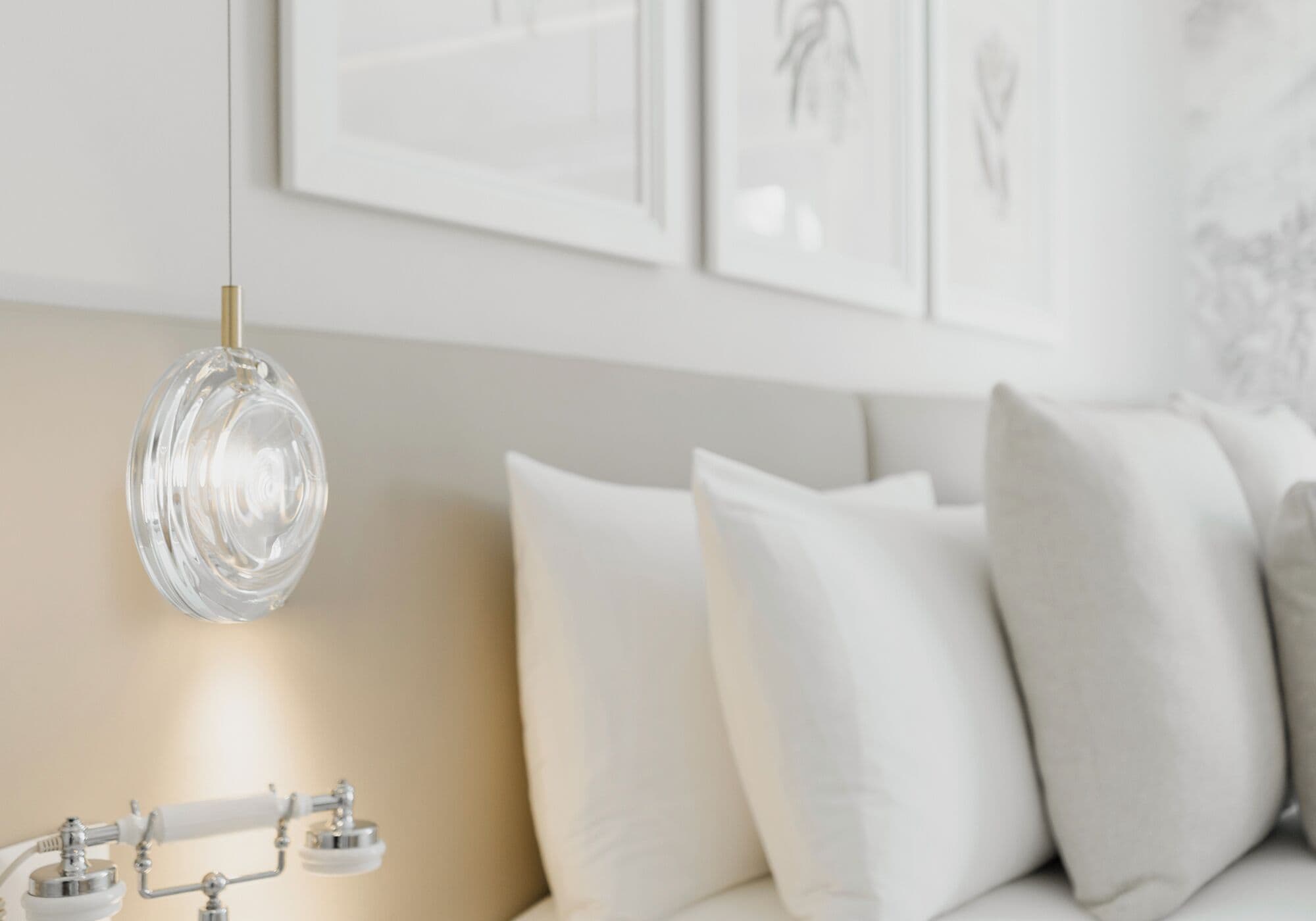 A modern living room with a clear glass pendant light, a beige sofa with white cushions, and framed artwork on the wall.