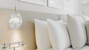 Uma sala de estar moderna com uma luminária pendente de vidro transparente, um sofá bege com almofadas brancas e quadros nas paredes.