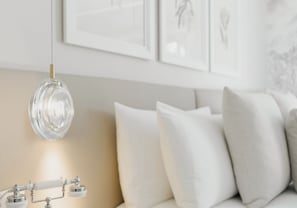Una sala de estar moderna con una lámpara colgante de vidrio transparente, un sofá beige con cojines blancos y obras de arte enmarcadas en la pared.
