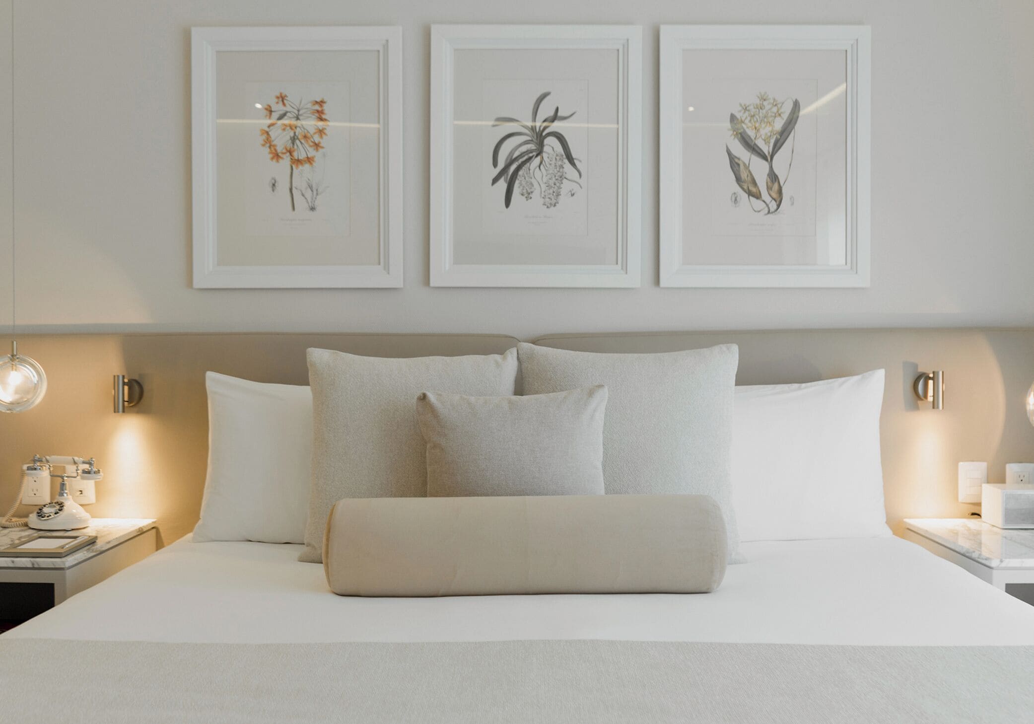 A hotel room with a large bed, two bedside tables, and three framed botanical prints on the wall.