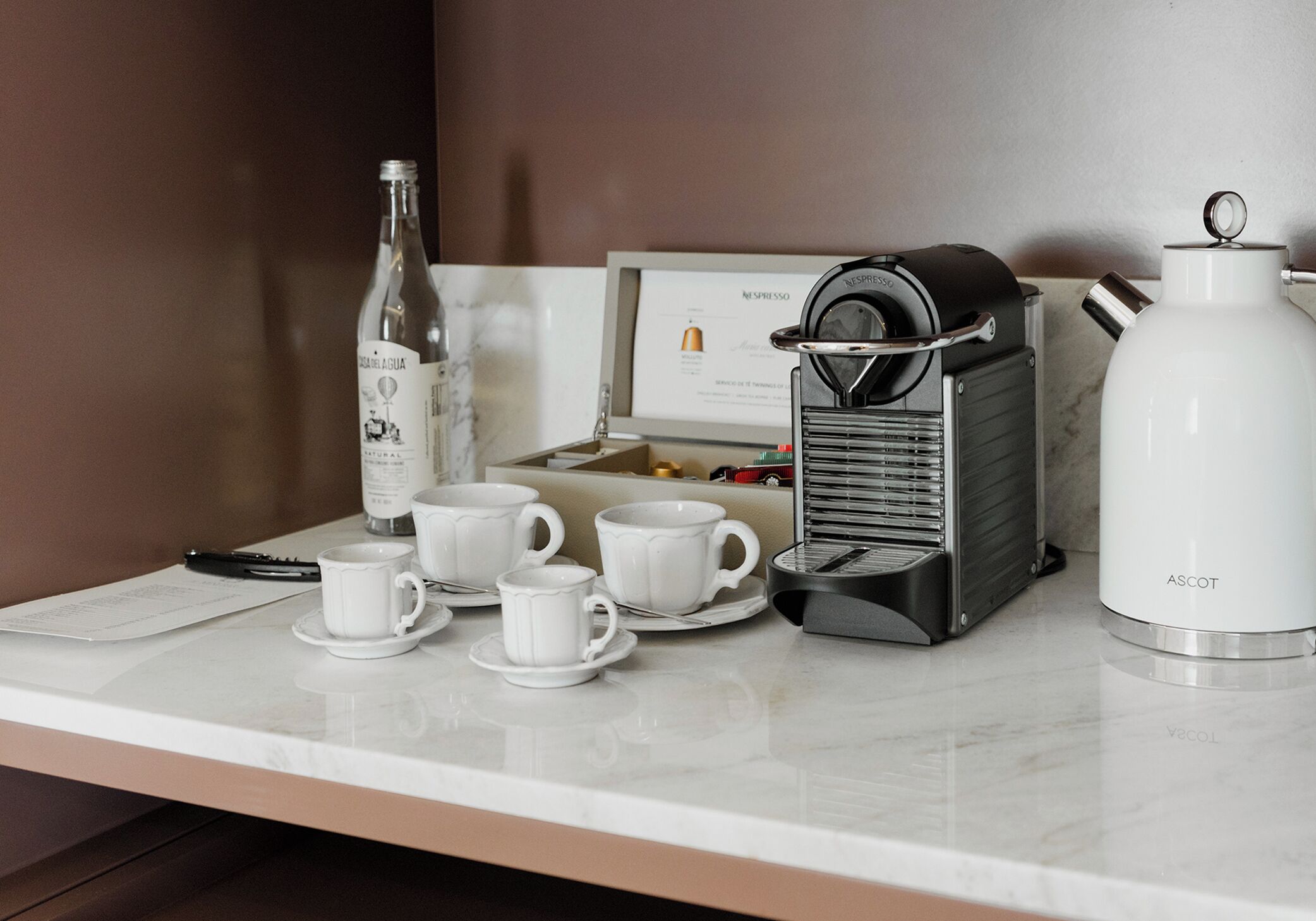 Un coin café équipé d’une machine Nespresso, de tasses, d’une bouteille d’eau et d’un menu.