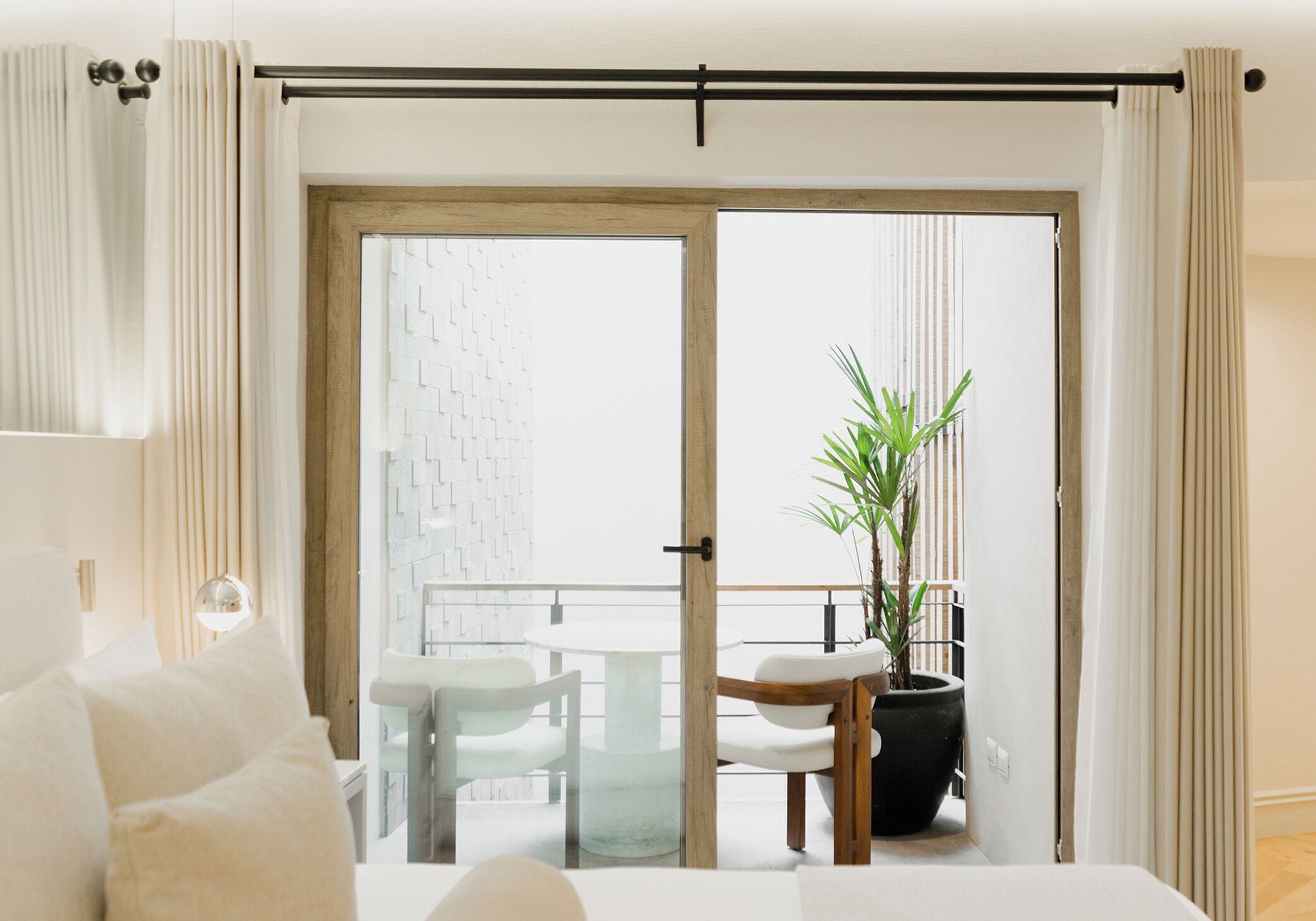 A hotel room with a bed, a balcony with a table and chairs, and a potted plant.