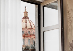 A view through a window of a building with a prominent dome and a statue on top.