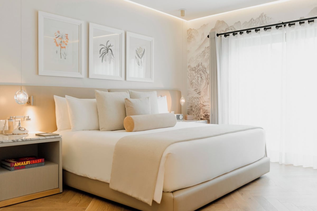 Un dormitorio moderno con una cama grande, mesitas de noche y una obra de arte botánica enmarcadas.