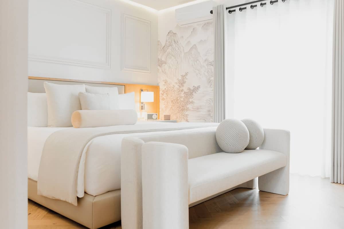 Een moderne slaapkamer met een groot bed, een nachtkastje met een lamp, en uitzicht op een berglandschap door het raam.