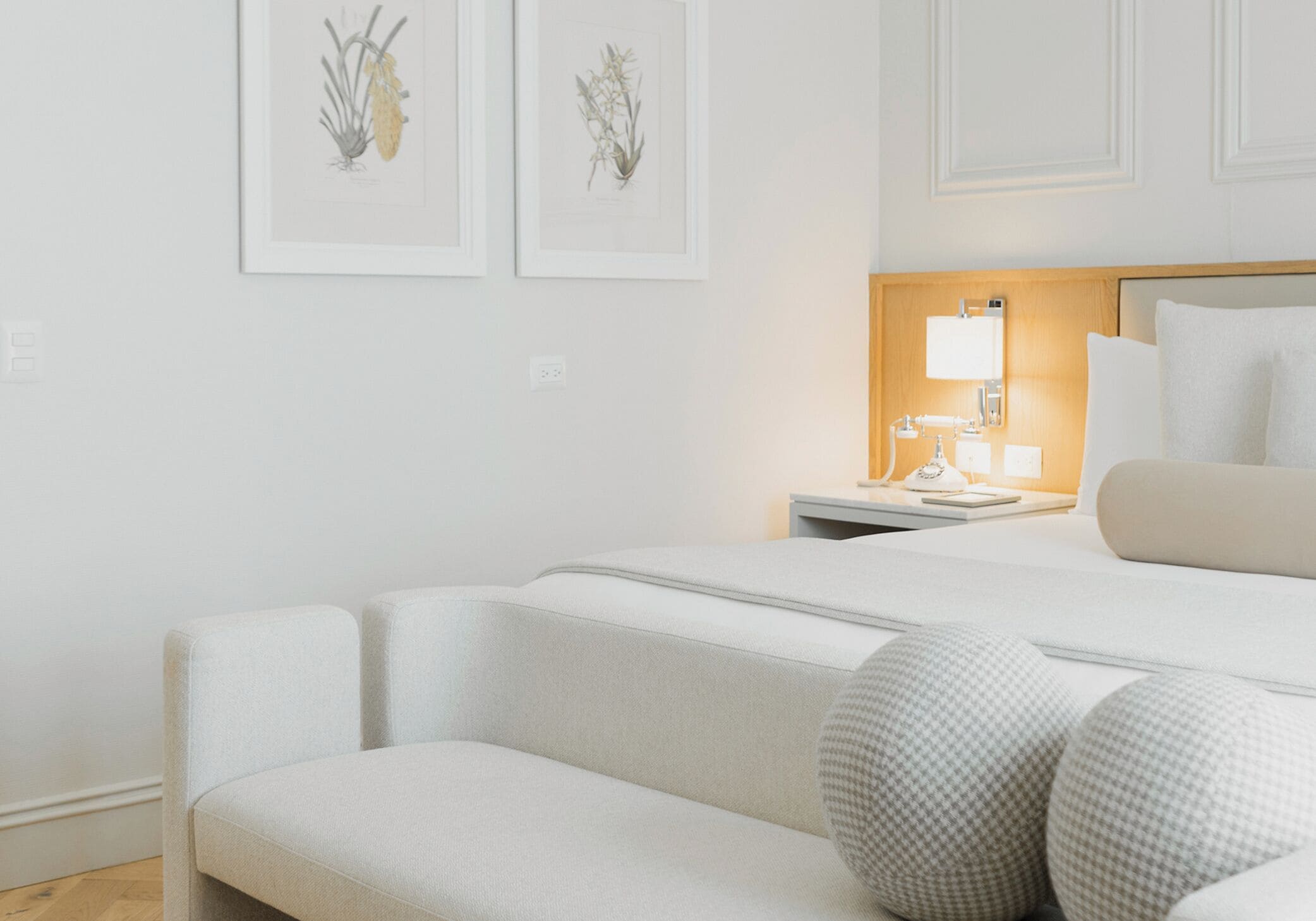 Ein Hotelzimmer mit einem Bett, einem Nachttisch mit Lampe, einem Sessel und zwei gerahmten Pflanzenbildern an der Wand.