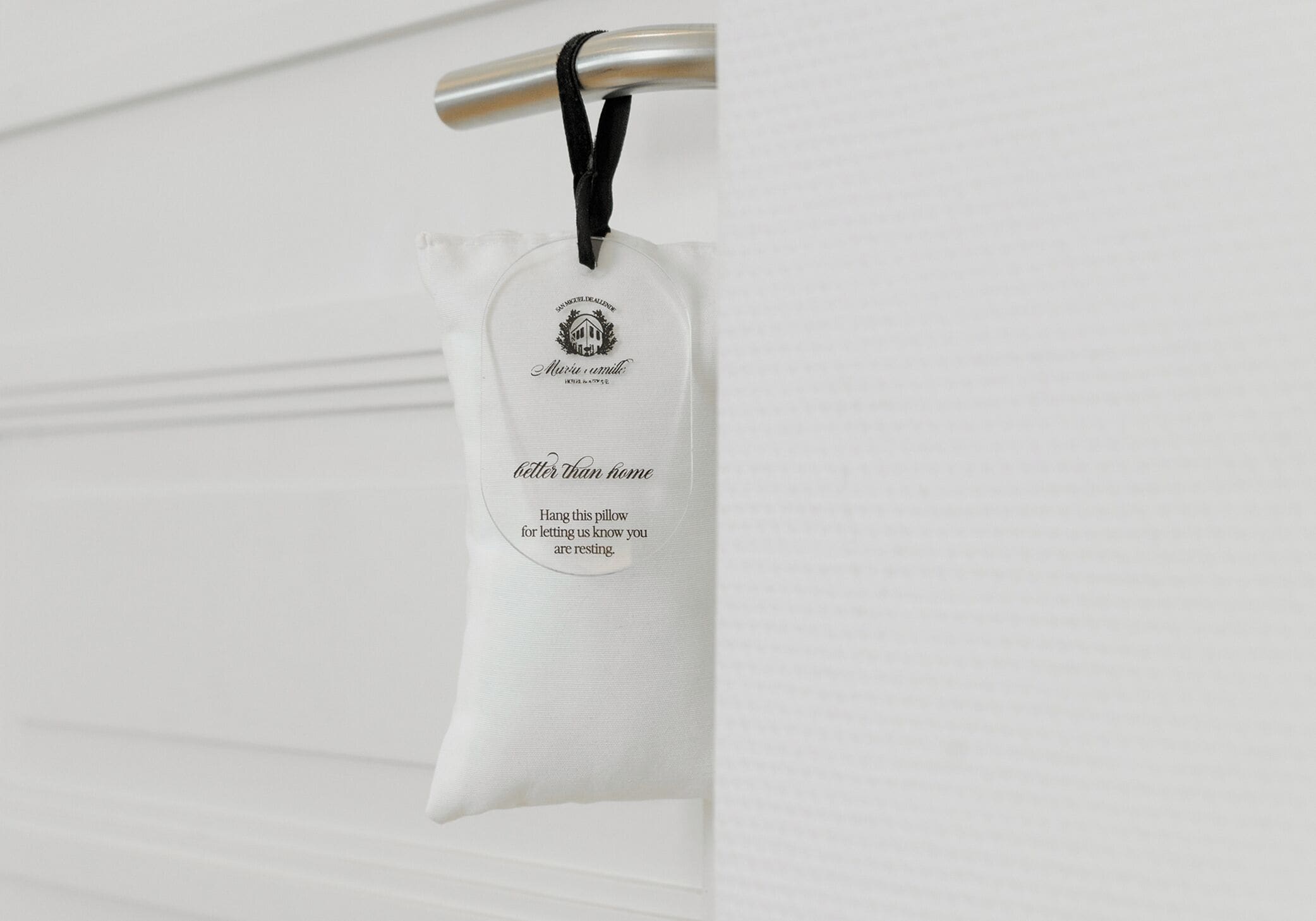 Een wit kussen met een label dat hangt aan een metalen bevestiging op een witte deur.