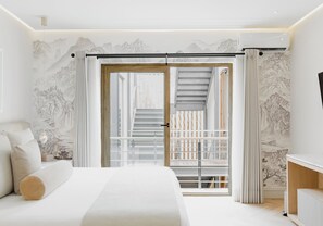 Un dormitori modern amb un llit gran, una porta corredissa de vidre que dona a un balcó, i obra tradicional a la paret.