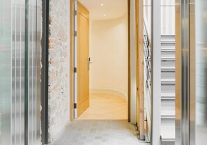 A corridor with a wooden door, a white wall, and a tiled floor.