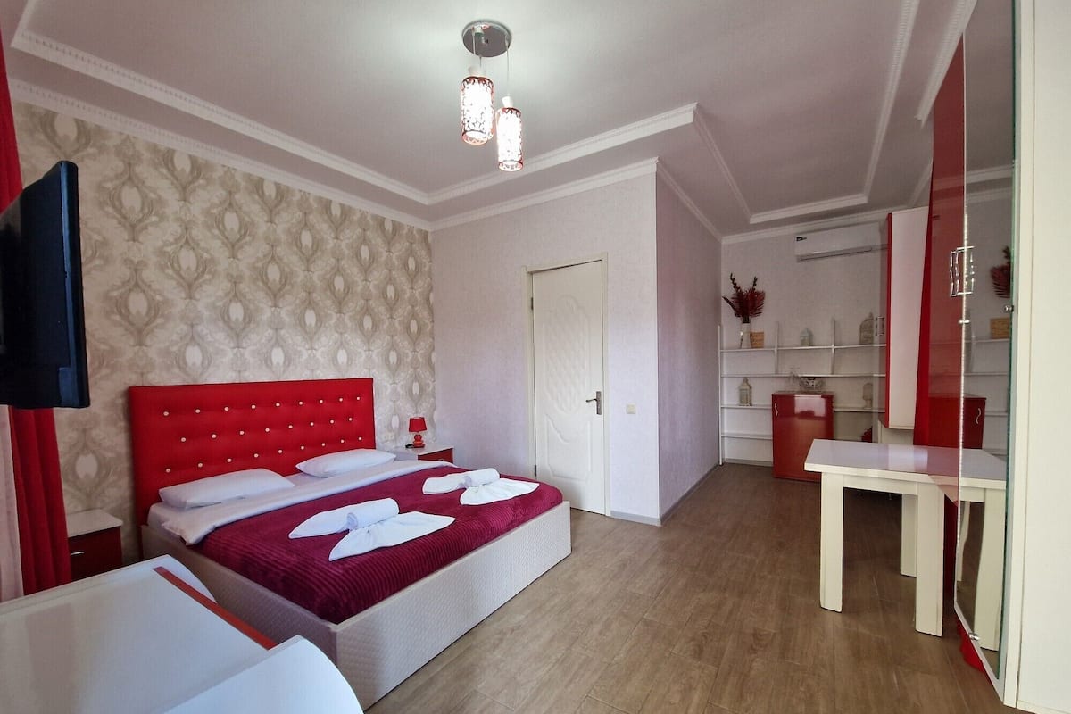 Ein Hotelzimmer mit einem roten möblierten Bett, einem weißen Nachttisch, einer roten Lampe und einem weißen Kleiderschrank.