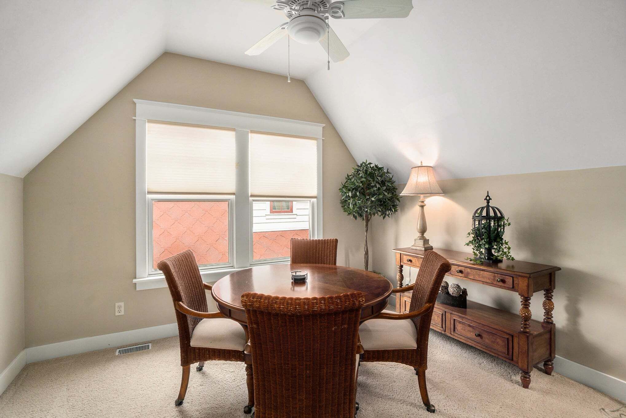 Un coin repas comprenant une table ronde, quatre chaises, un ventilateur de plafond, une lampe et une petite plante.