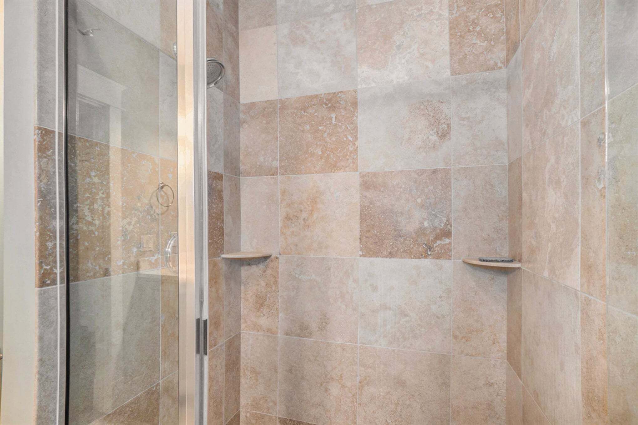 Une douche avec des portes en verre et des carreaux de couleur beige.