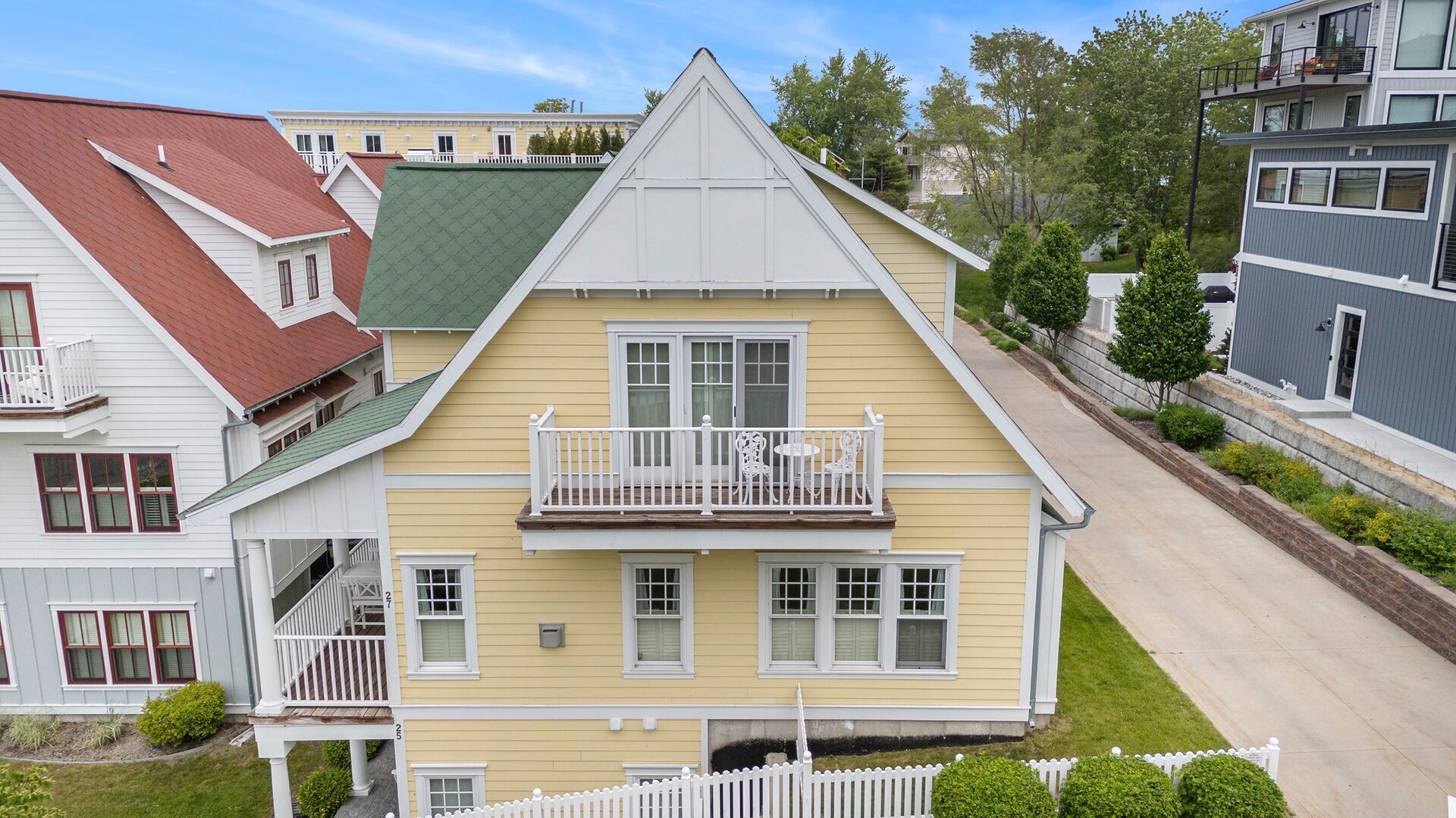 A two-story house with a green roof, a balcony with white railings, and a small front yard.