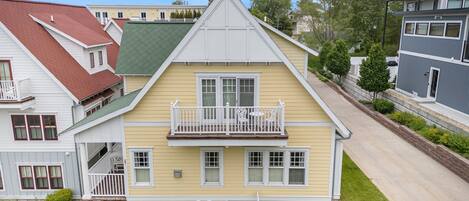 A two-story house with a green roof, a balcony with white railings, and a small front yard.