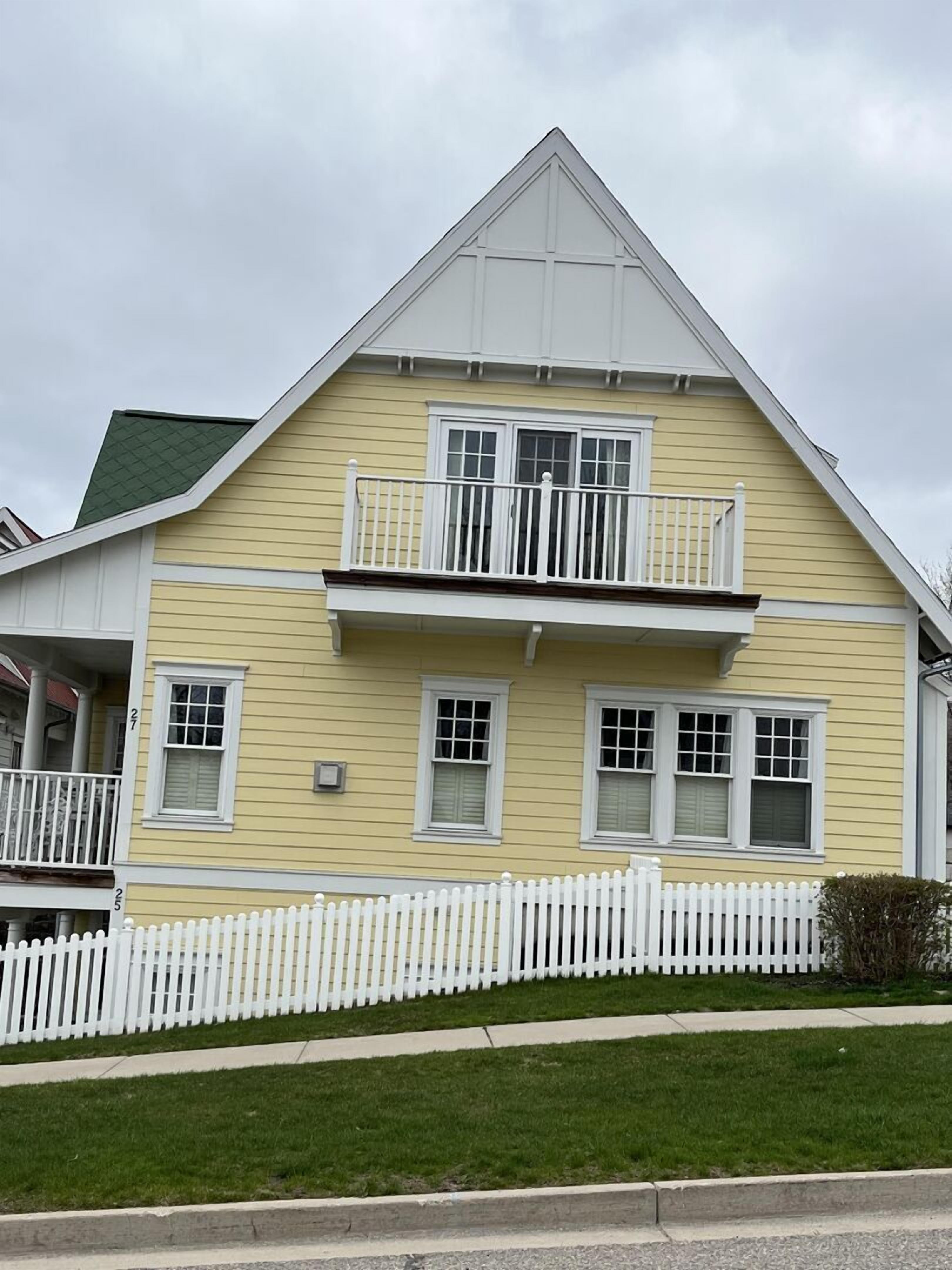 A two-story house with a white picket fence, a balcony on the second floor, and a green roof.