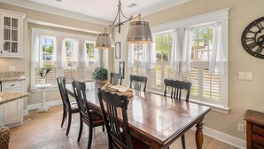 A dining area with a wooden table, chairs, pendant lights, and large windows with white curtains. - Family-Friendly 3BR Condo Grand Haven 27 (Grand Haven)